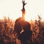 Side view of graceful woman leaning back with raised leg while dancing between shrubs in countryside in back lit