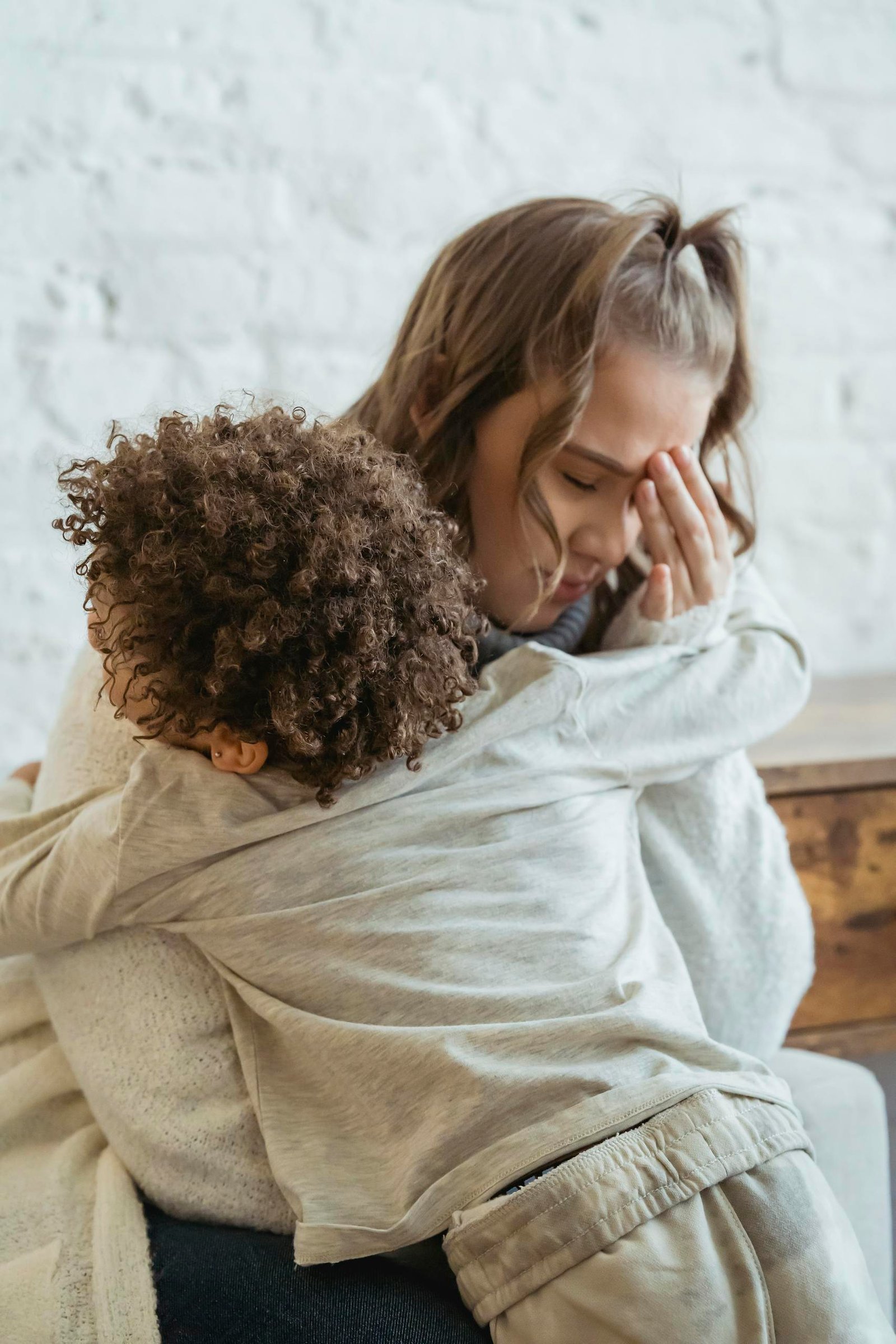 Tired lady with hand on head embracing with child